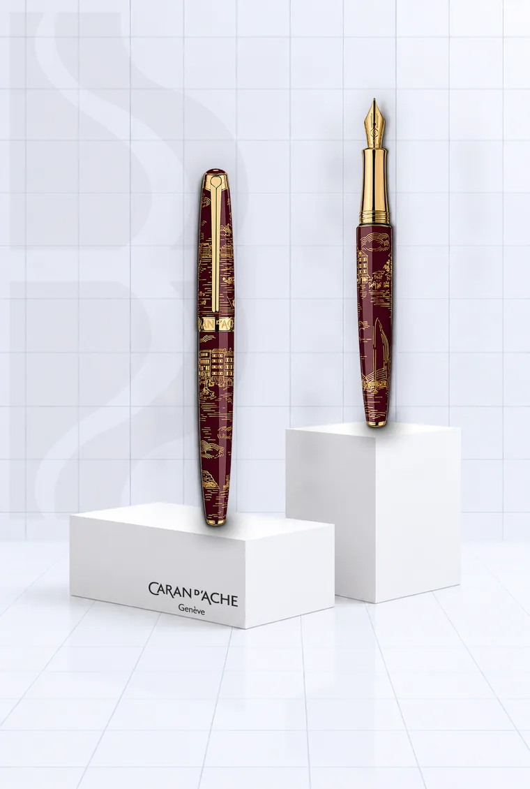Deux stylos plume Caran d’Ache laqués grenat à gravures dorées, sur des socles blancs